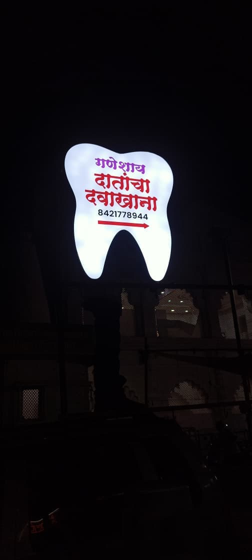 Illuminated tooth-shaped street sign marking Ganeshay Dental Clinic in Maliwada